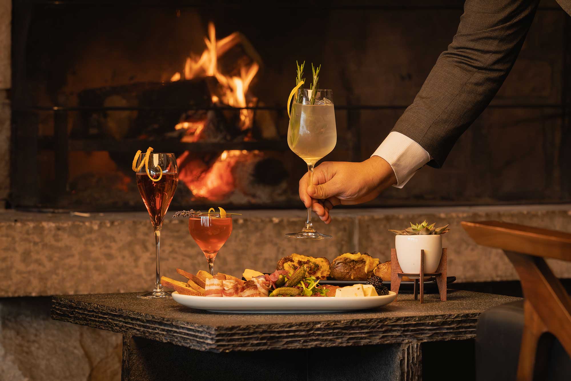 cocktails and charcuterie board in front of restaurant fireplace at Stanley's Kitchen & Bar in Jasper, Alberta