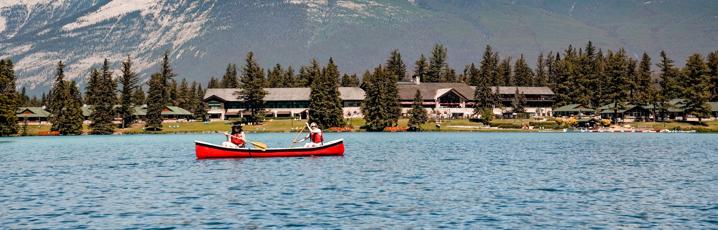 Two friends canoeing on Lac Beauvert with Fairmont Jasper Park Lodge in the background in the summer.