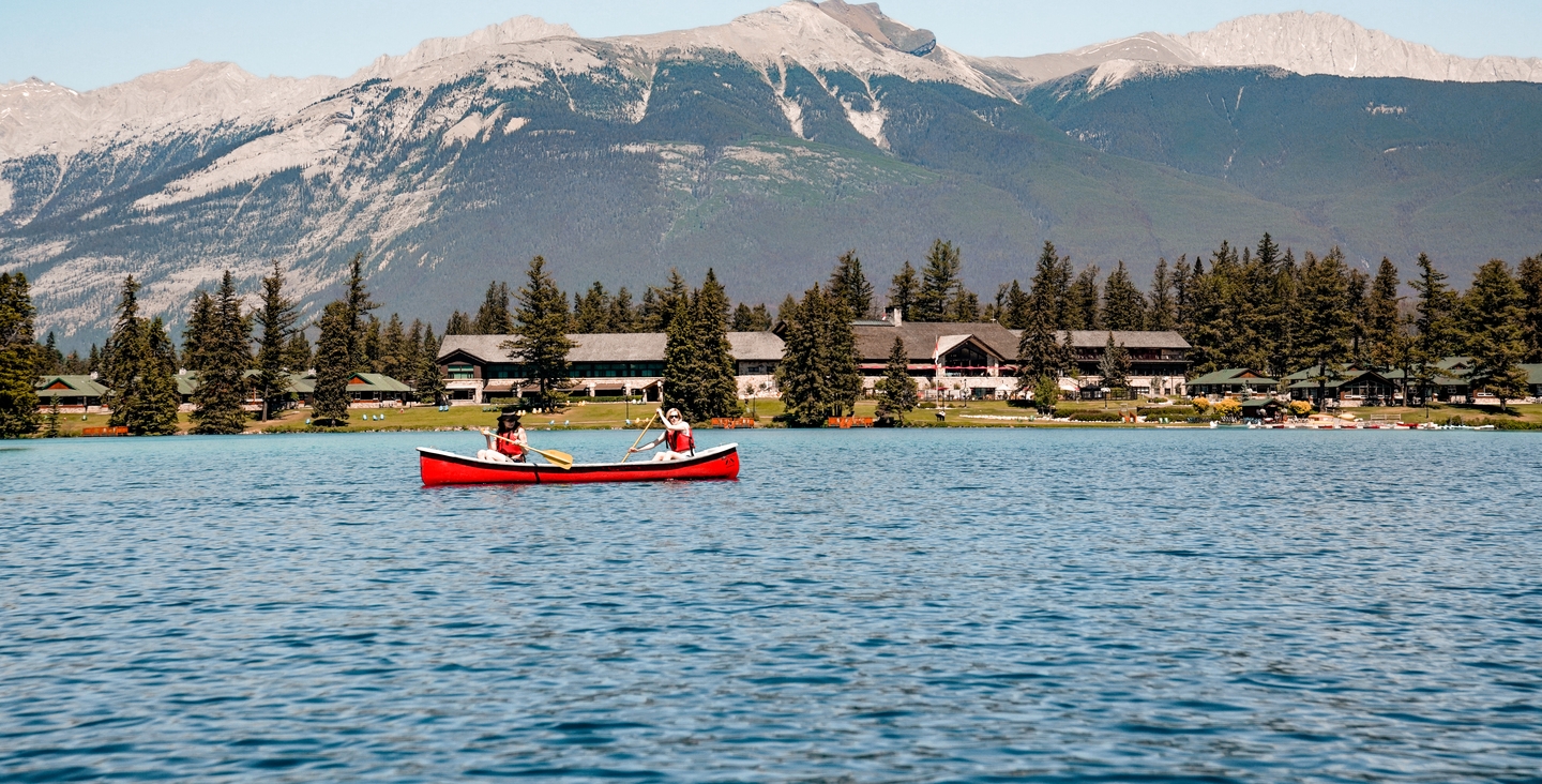 Two friends canoeing on Lac Beauvert with Fairmont Jasper Park Lodge in the background in the summer.