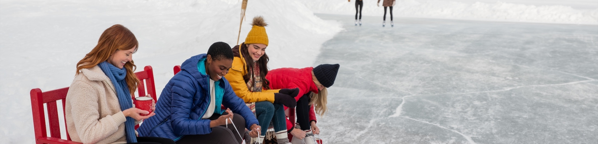 Friends in skates sitting on a bench by a frozen lake