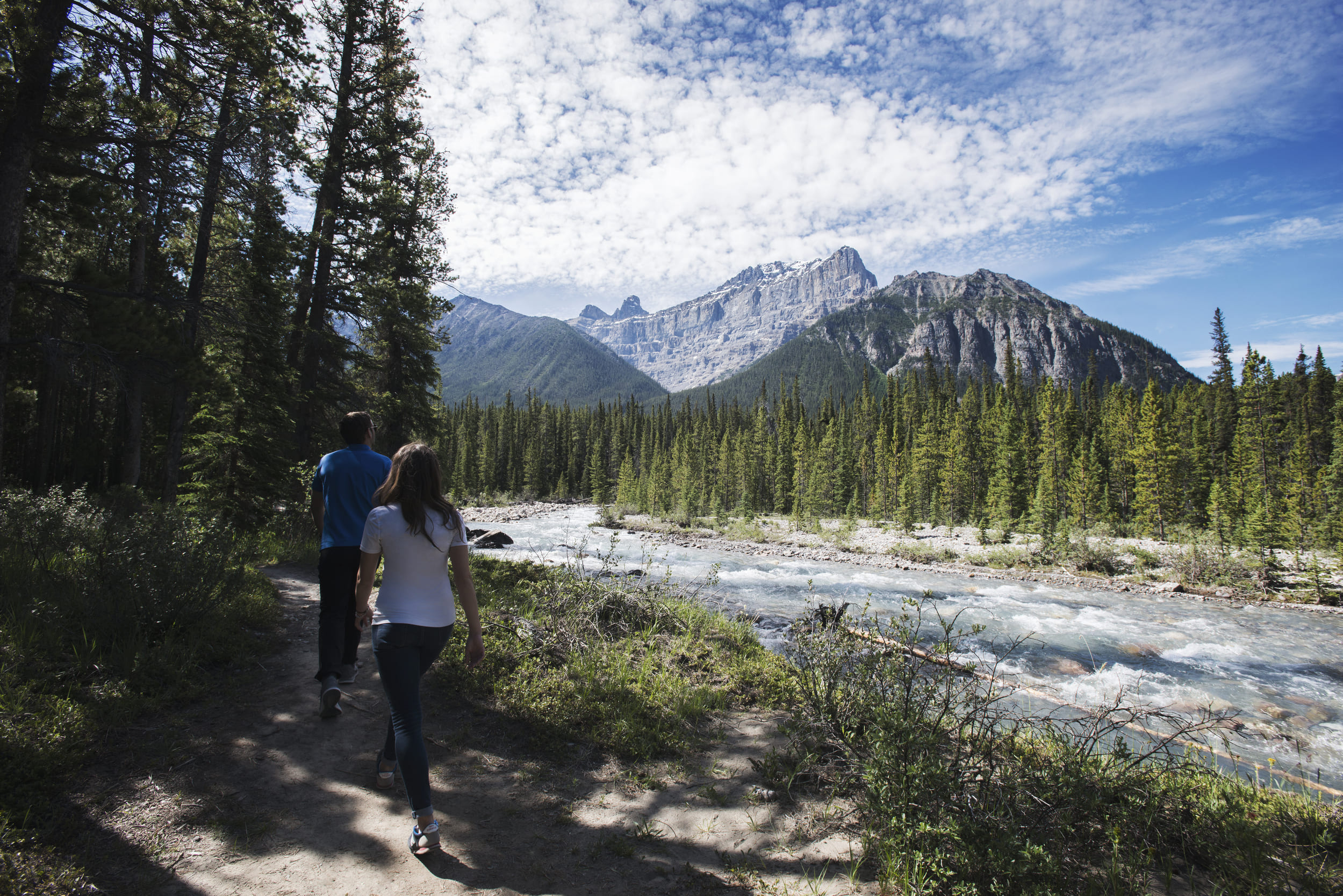 couple hiking along river trail with mountains
