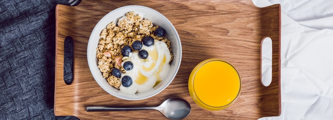 Photo of an in-room dining tray with a spoon, glass of orange juice and a yogurt bowl.