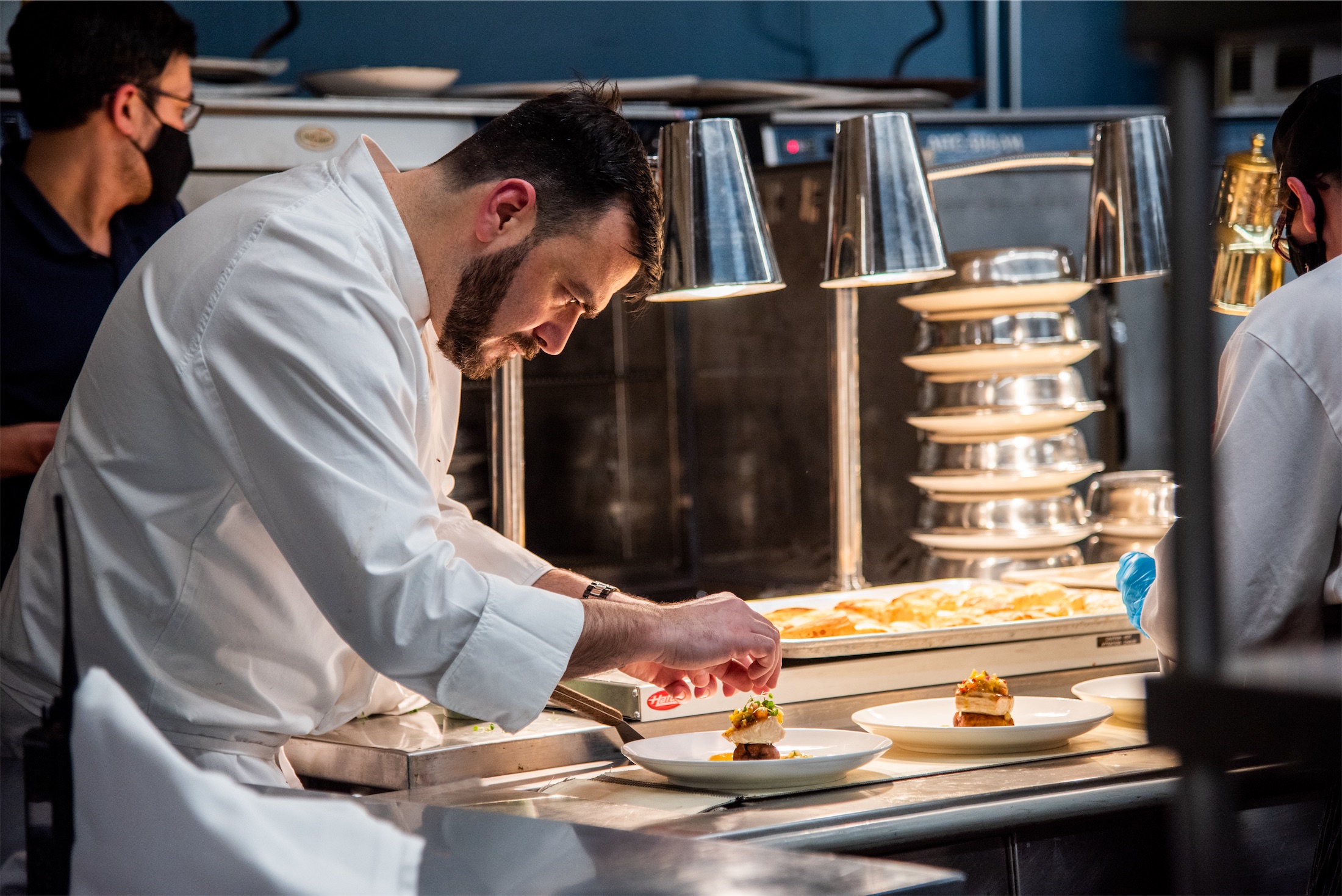 A chef in a professional kitchen adding final touches to a dish
