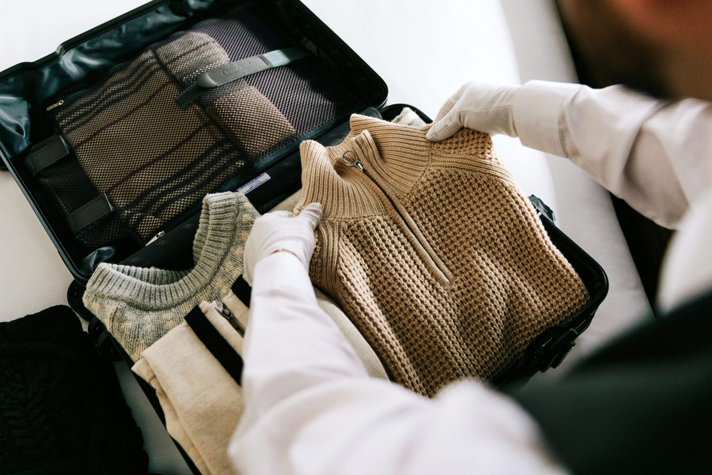 closeup of packing a suitcase with white gloves on