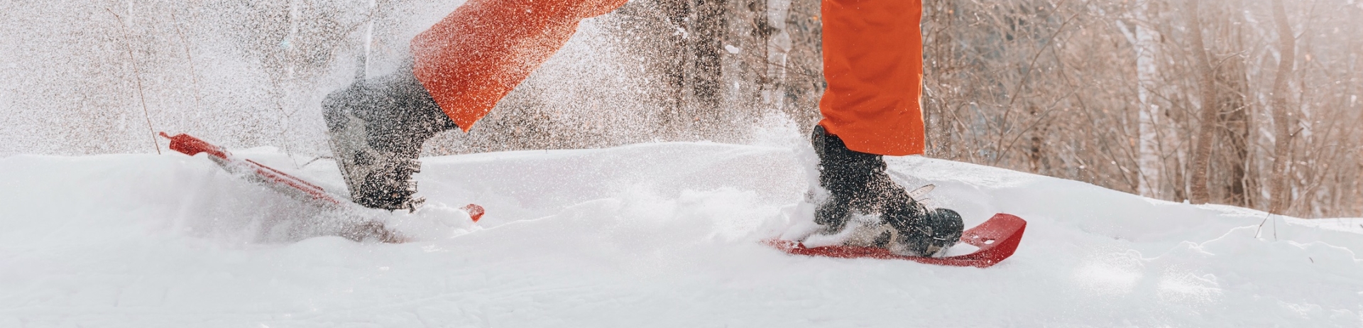 A person in orange snow pants showshoeing in the woods