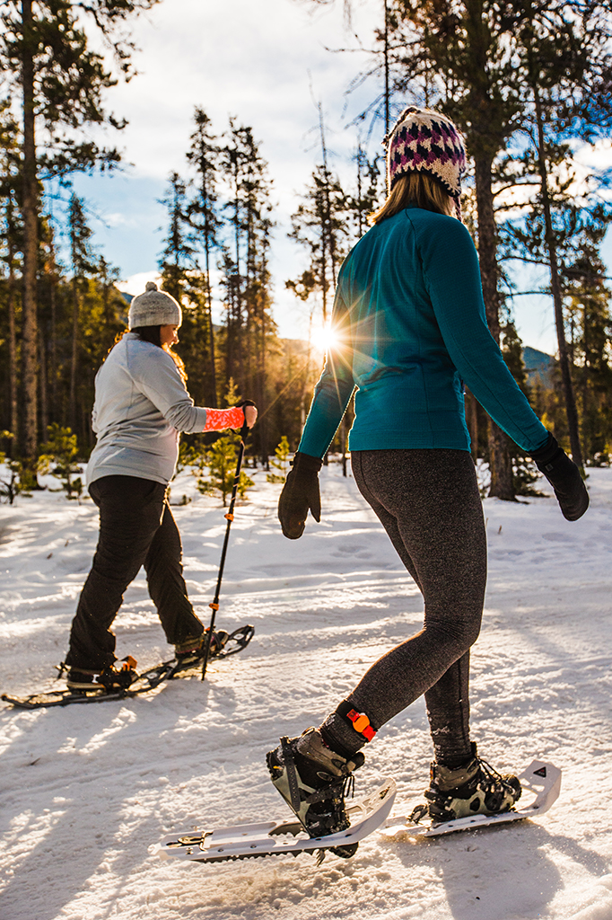 two woman snowshoeing through woods