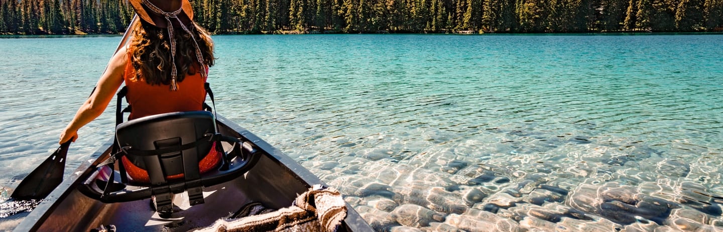 woman in canoe on blue lake water and mountains
