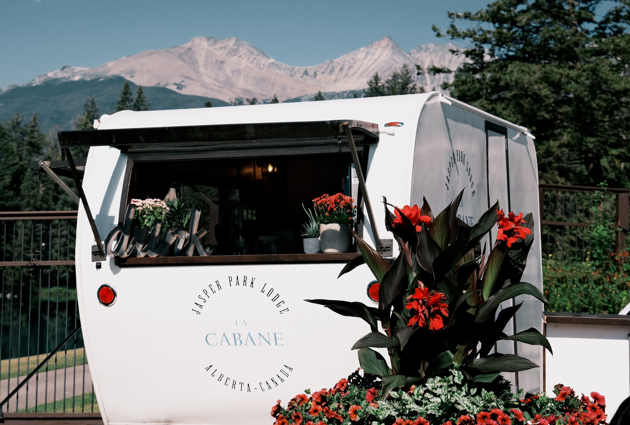 A cocktail camper sits open with mountains in the background and florals surrounding it at Jasper Park Lodge.