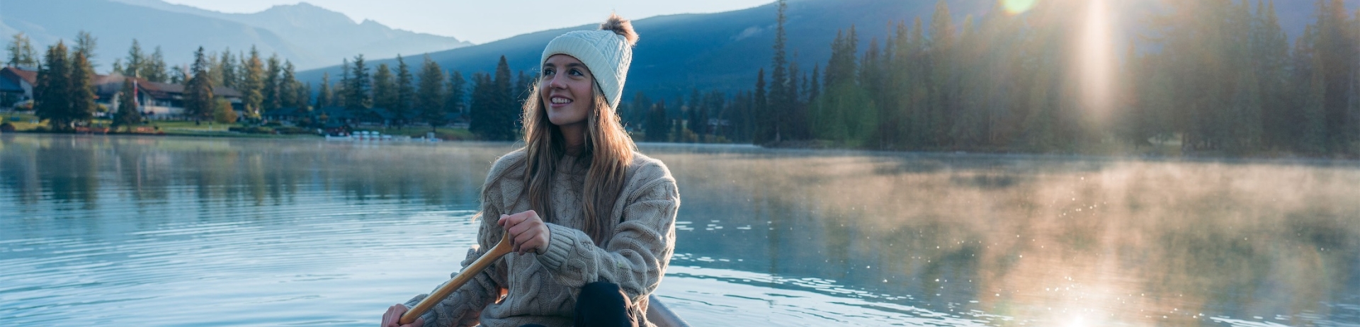 woman paddling across lake with white winter hat