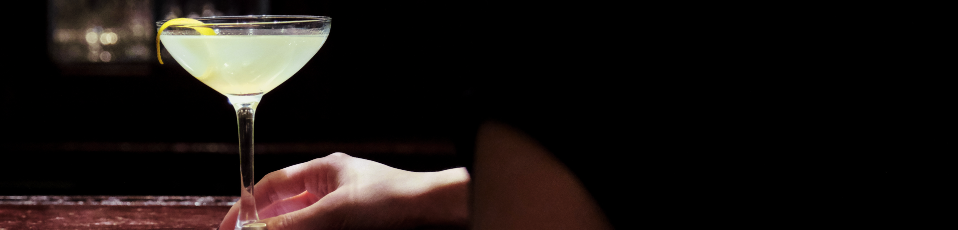 Woman sitting at the bar facing away reaches of her drink sitting on the bar top of Orso Trattoria in Jasper Park Lodge