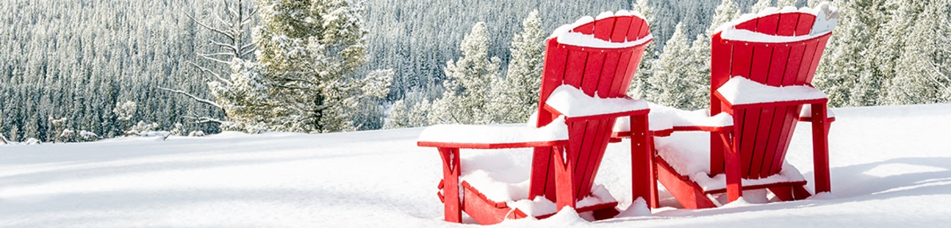 Two red Adirondack chairs in the snow with a view of mountains