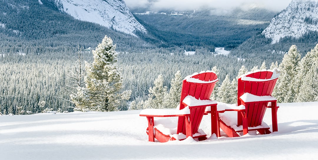Two red Adirondack chairs in the snow with a view of mountains