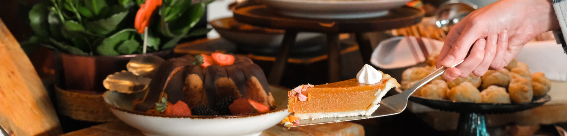 Holiday meal on a table scape with a hand serving a slice of pumpkin pie.