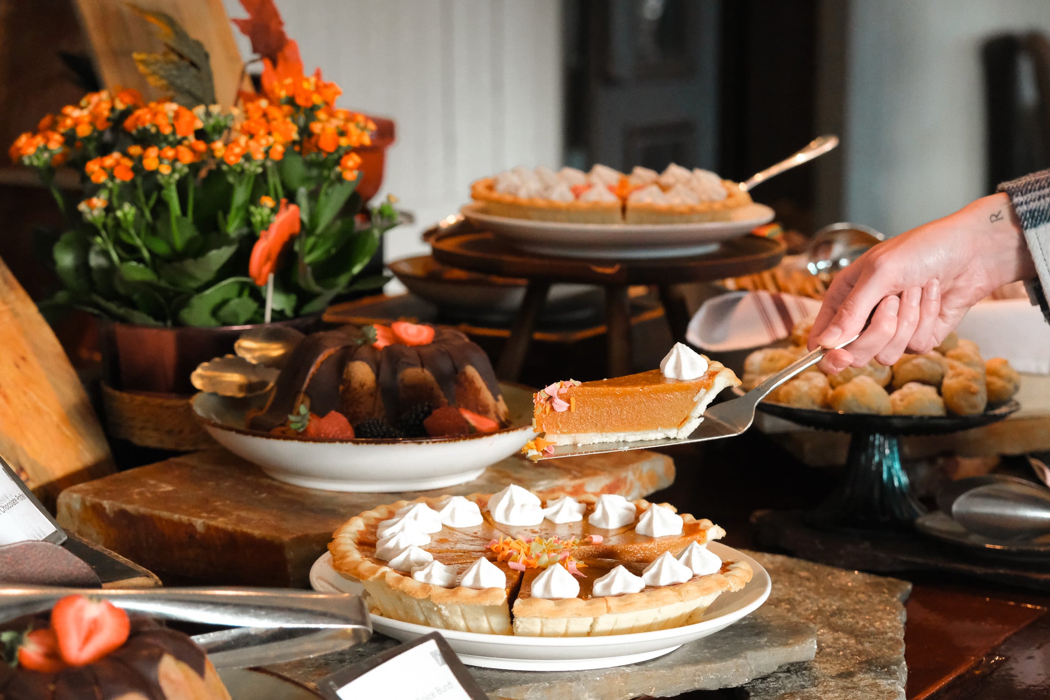 Holiday meal on a table scape with a hand serving a slice of pumpkin pie.