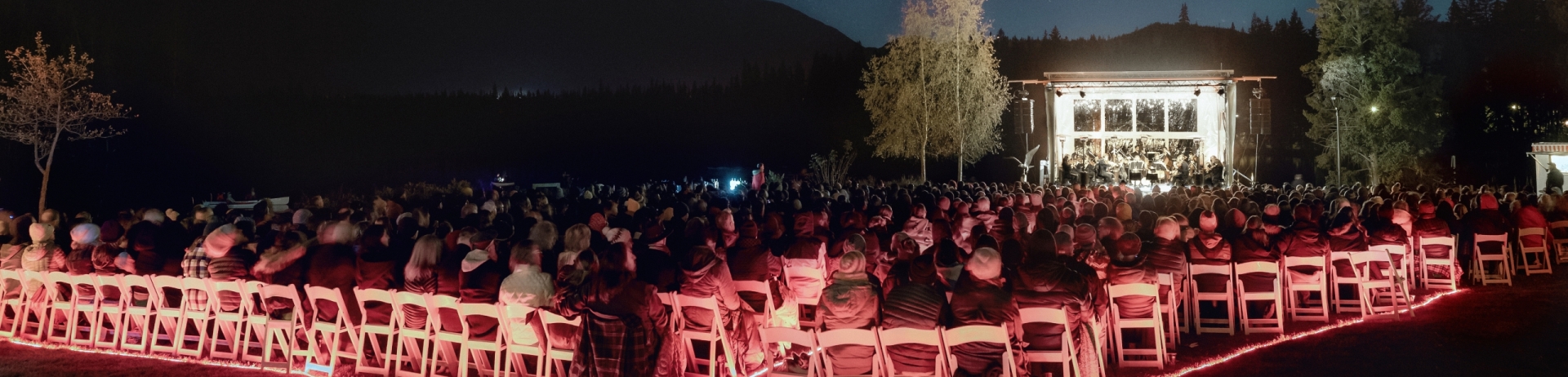 Orchestra setting lit up in red lights while stars above are in the night sky at Jasper Park Lodge's Symphony Under the Stars