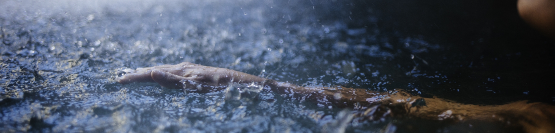 Arm extended in a pool while rain drops splatter the service of the water. Fairmont Spa asset.