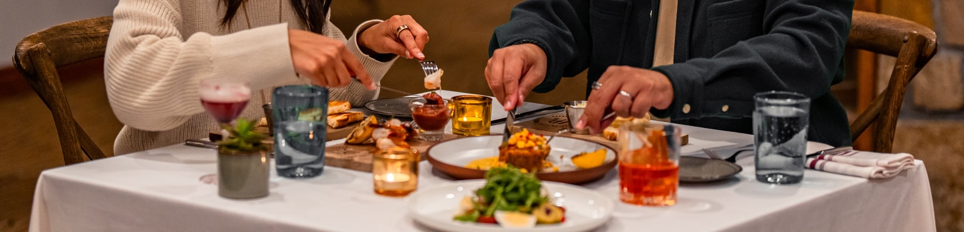 Couple dining at a table for two with a lots of food and cutting into their dishes at The Nook at Fairmont Jasper Park Lodge