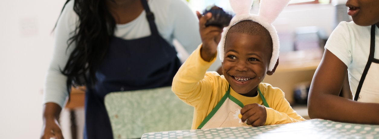 Young mother pretends to want to steal sons cupcake that he is eating. He holds it away from her giggling. Easter celebrations with family.