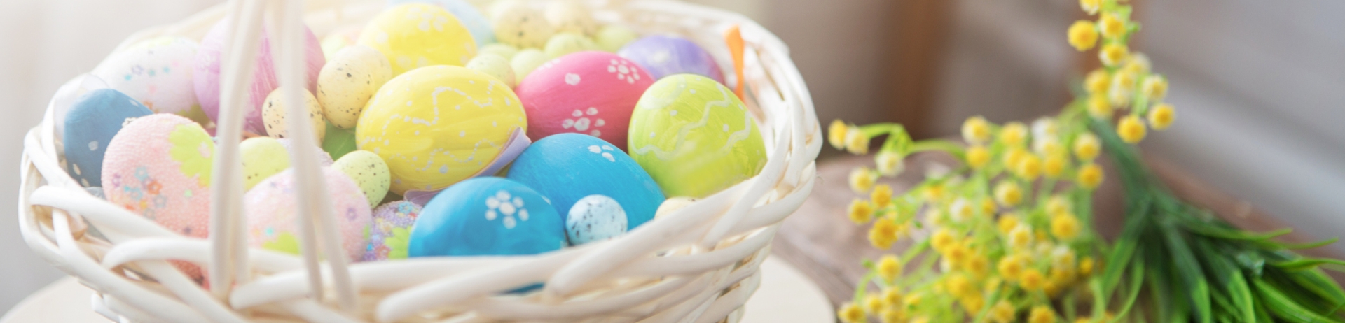 Close up painted Easter eggs in a basket and paintbrush resting on a wood plank table.