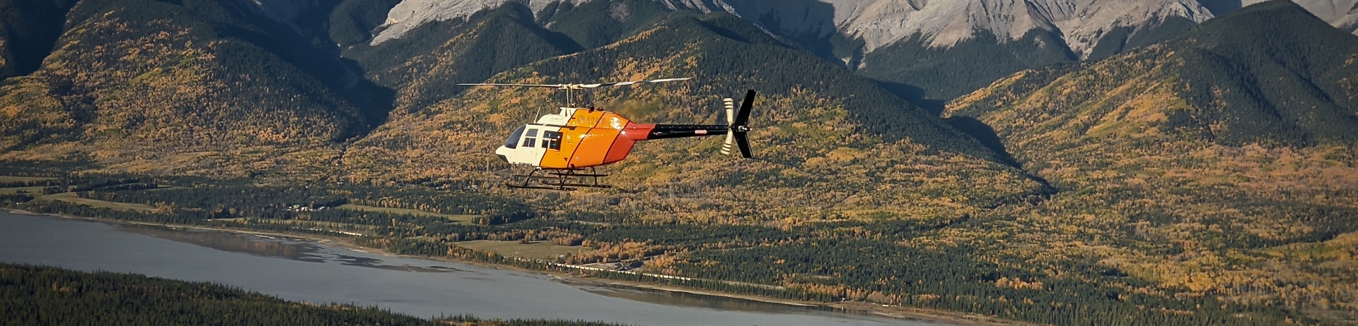 A helicopter flying over Jasper National Park with a mountain range in the background.