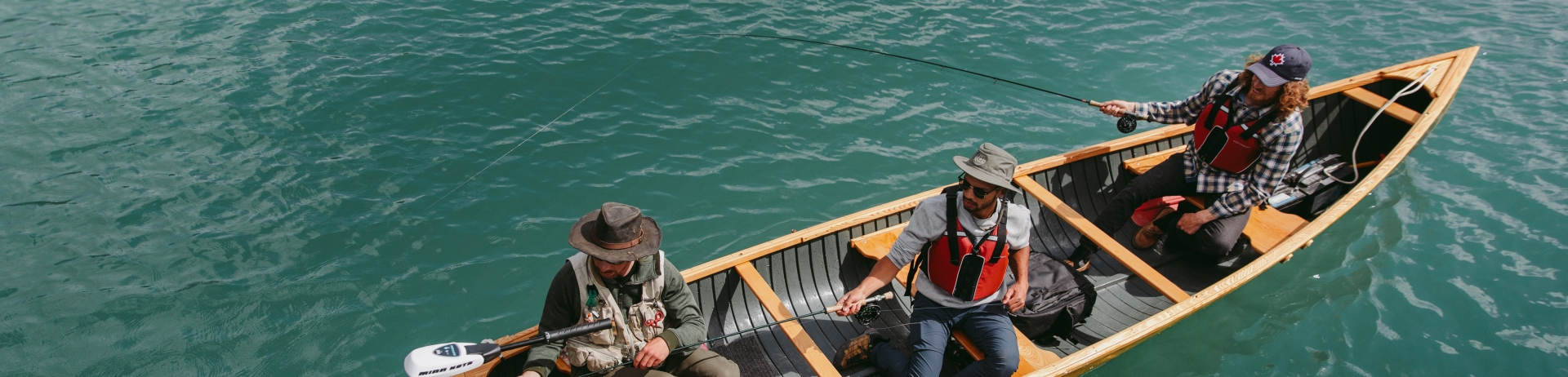 Three men in a boat fishing on a clear lake.