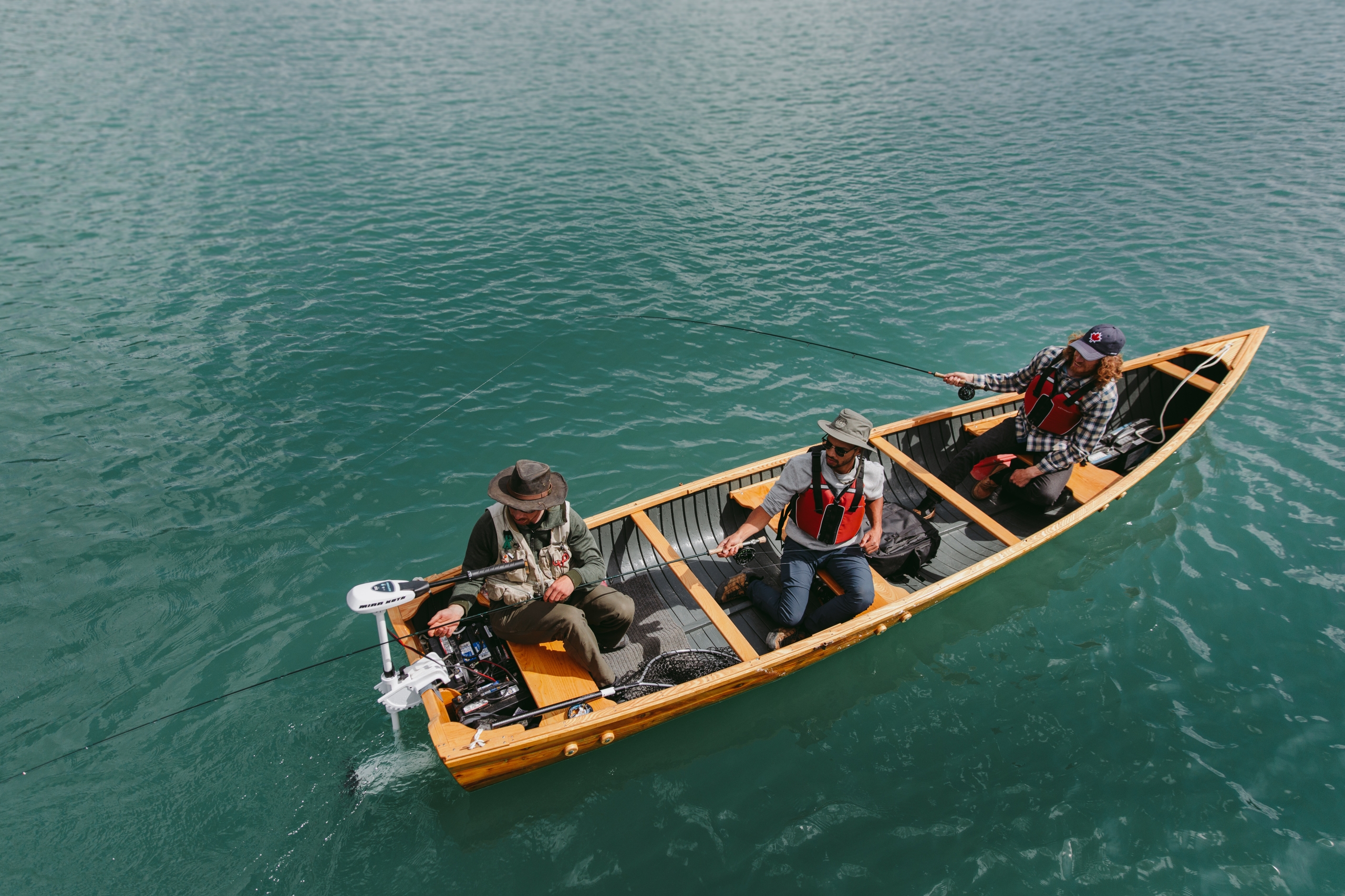 Three men in a boat fishing on a clear lake.