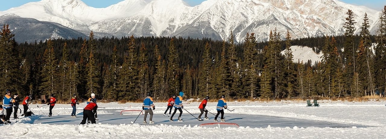 A group playing ice hockey on Lake Mildred at Fairmont Jasper Park Lodge with a scenic view of Lake Pyramid in the background.