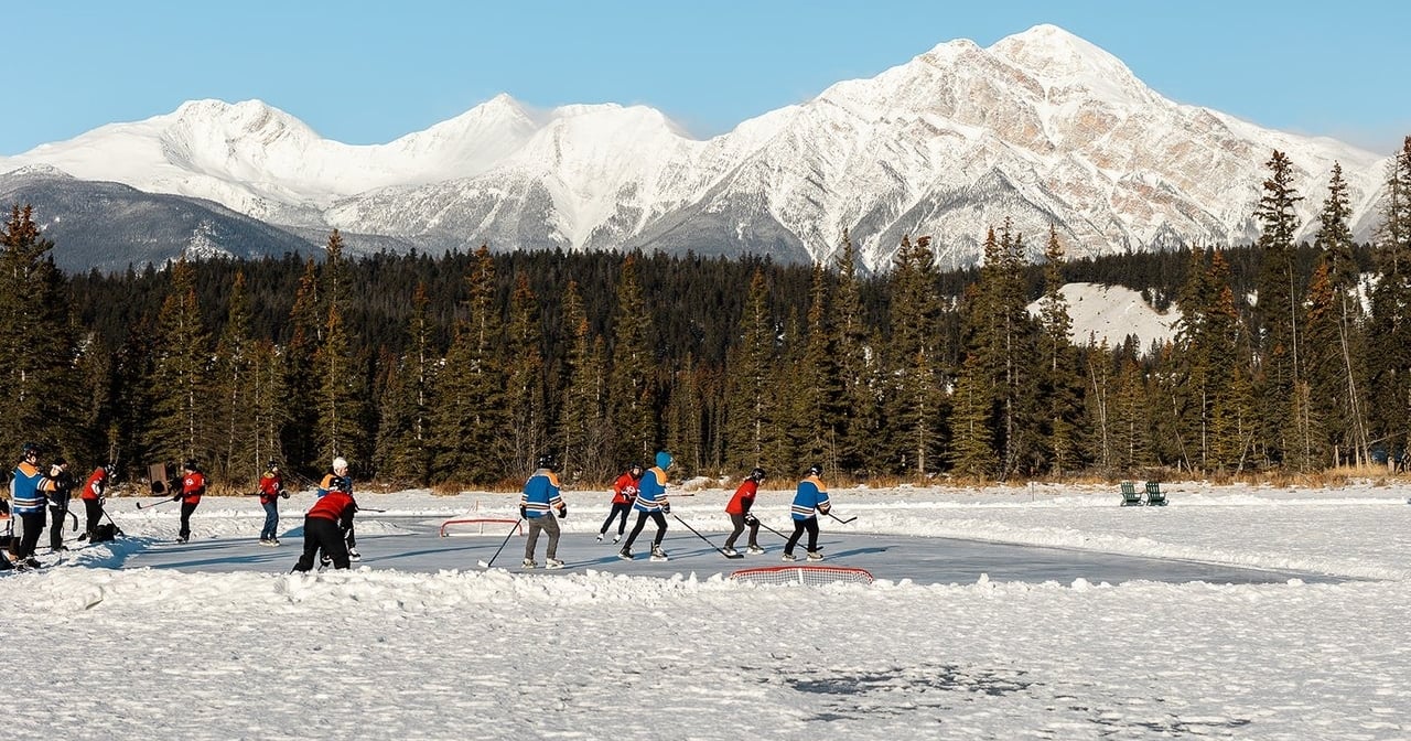 A group playing ice hockey on Lake Mildred at Fairmont Jasper Park Lodge with a scenic view of Lake Pyramid in the background.