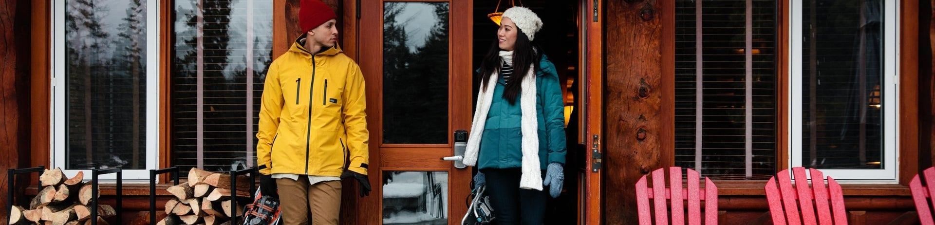 Couple standing outside a cabin in winter layers holding snowshoes