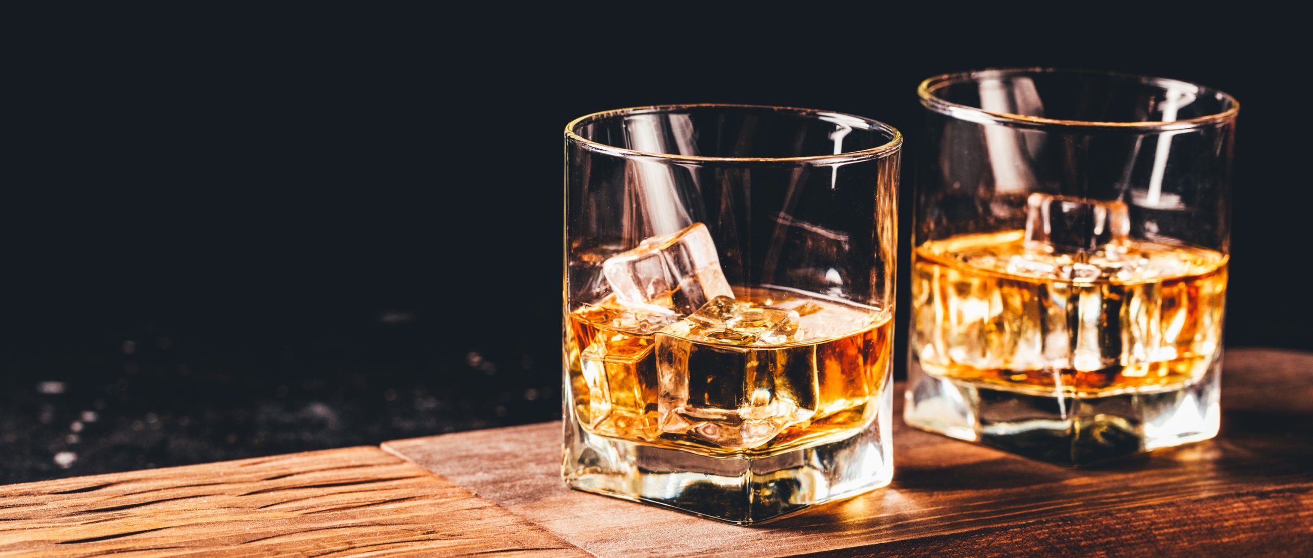 2 Glasses of Whiskey on a wooden countertop, served on the rocks.