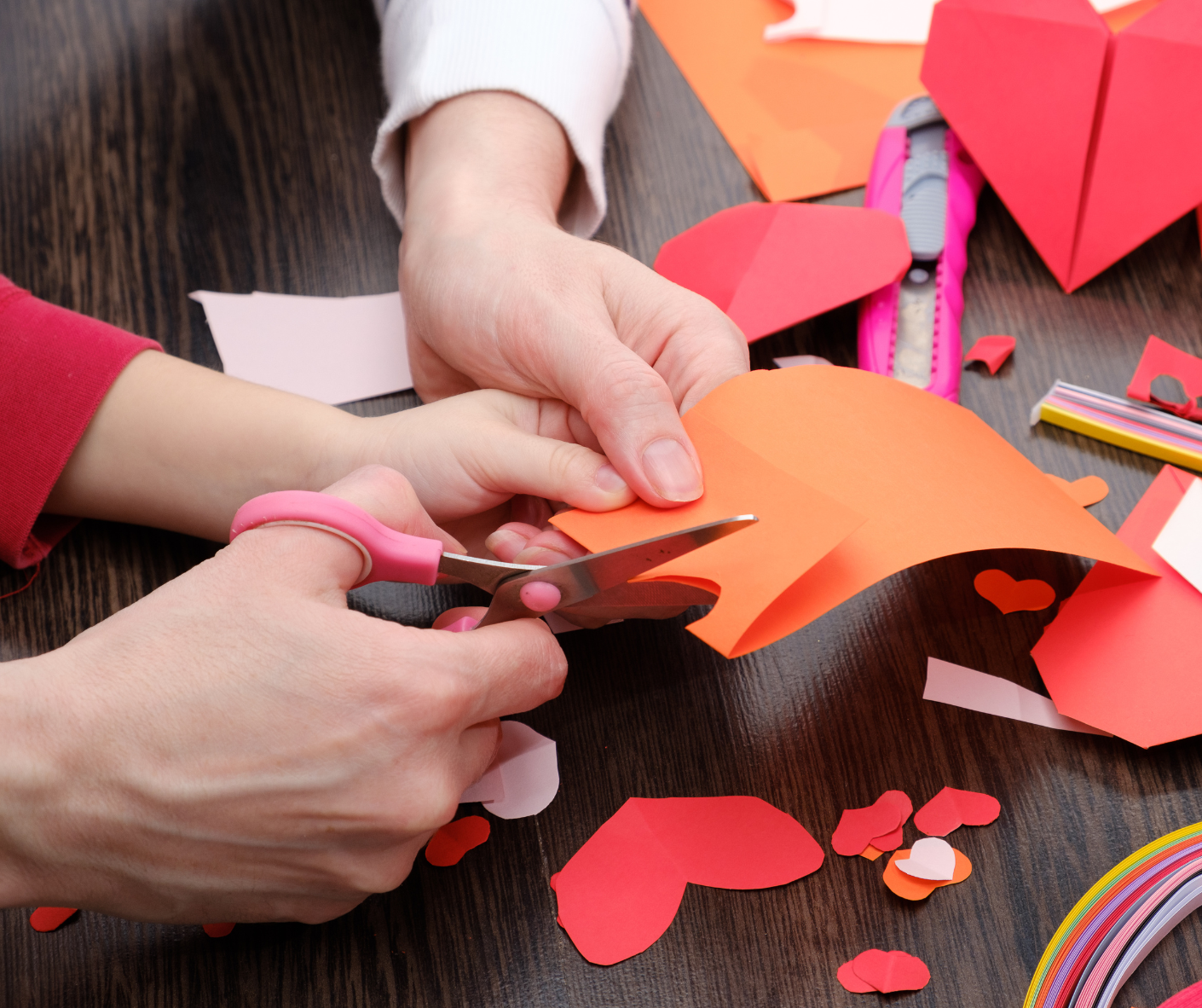 Family using scissors to cut out a heart shape from construction paper for a craft.