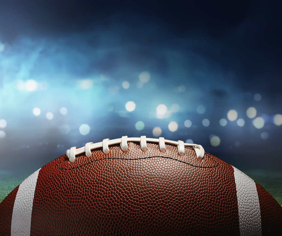 A football in a football field filled with bright, game day lights.