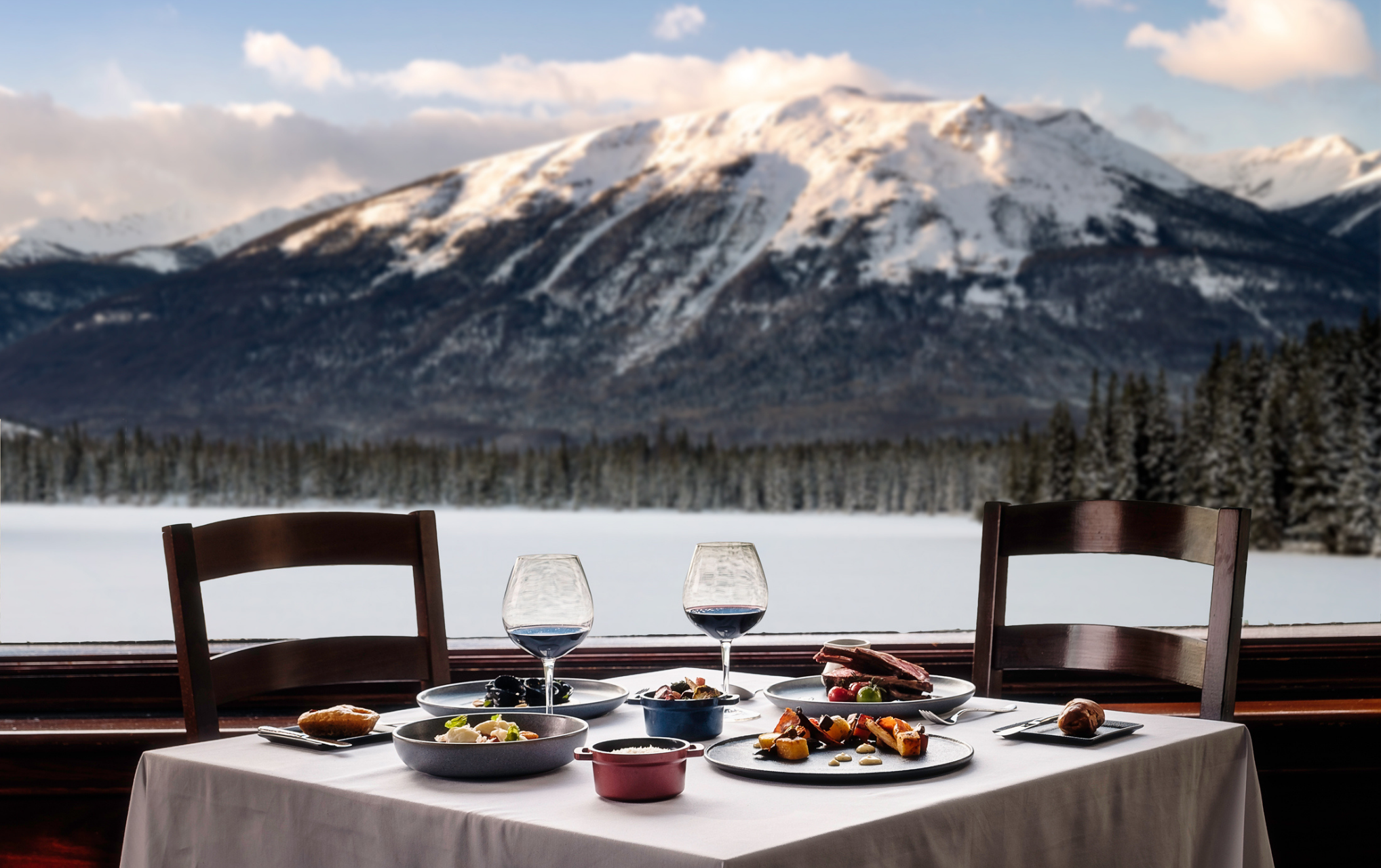 A full table setting including meal, wine, and a stunning winter mountain view.
