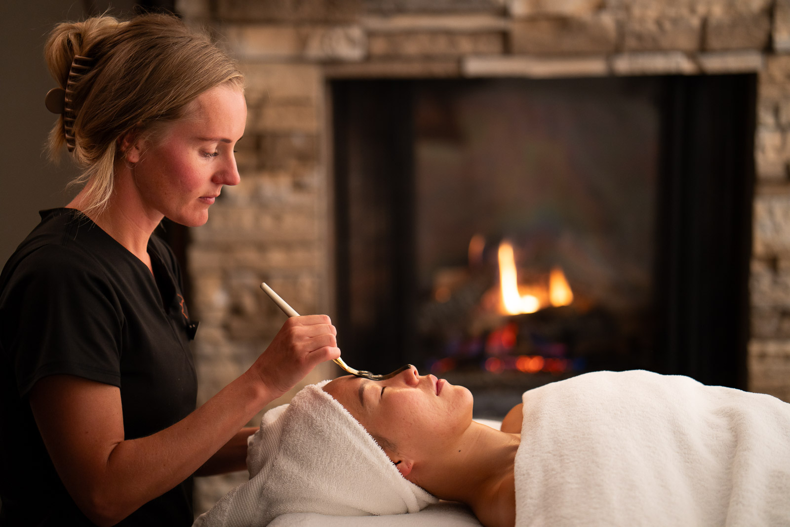 A woman receiving a facial in front of a fireplace at the Spa