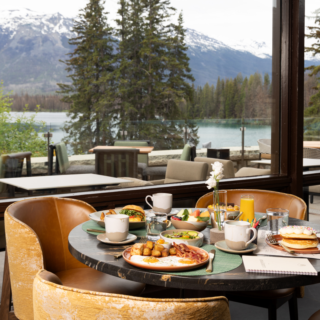A meal on a table in a restaurant in front of a window with a mountain and alpine view.