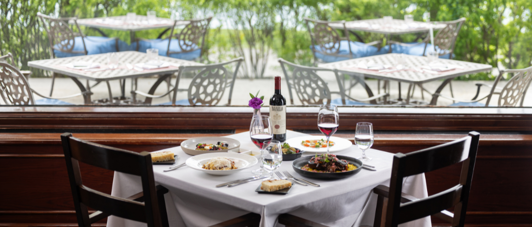 Dinner and wine on a table set in front of a window with greenery in the background.