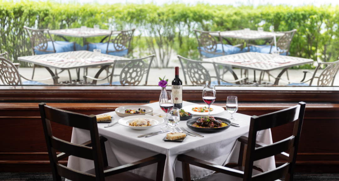Dinner and wine on a table set in front of a window with greenery in the background.
