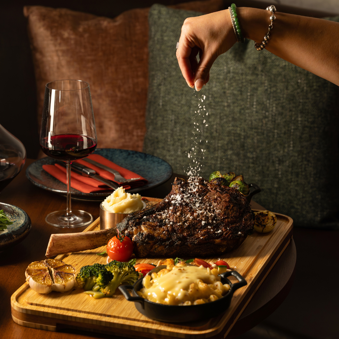 Woman's hand sprinkling salt on a cooked tomahawk steak.