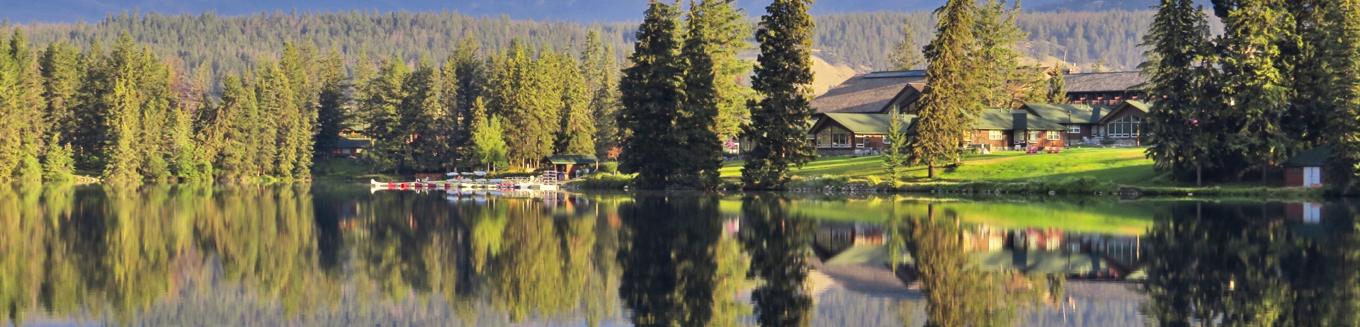 Scenic summer photo of Fairmont Jasper Park Lodge as seen from the golf course with a view of the boathouse and main lodge against the backdrop of Pyramid Mountain.