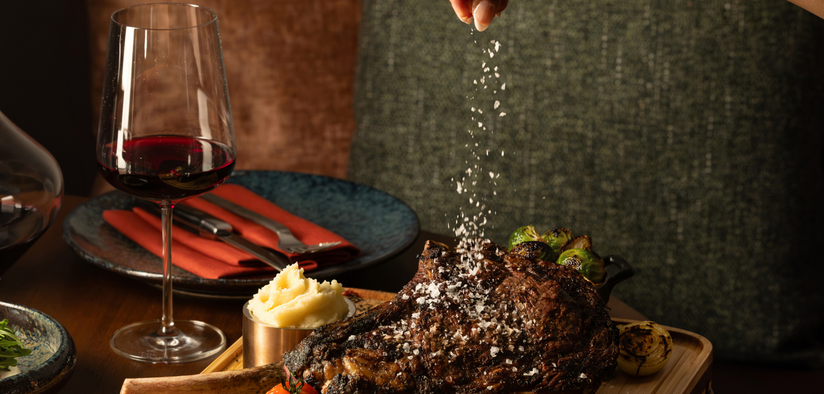 Woman's hand sprinkling salt on a cooked tomahawk steak.