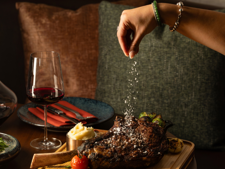 Woman's hand sprinkling salt on a cooked tomahawk steak.