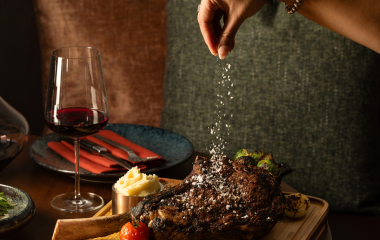 Woman's hand sprinkling salt on a cooked tomahawk steak.