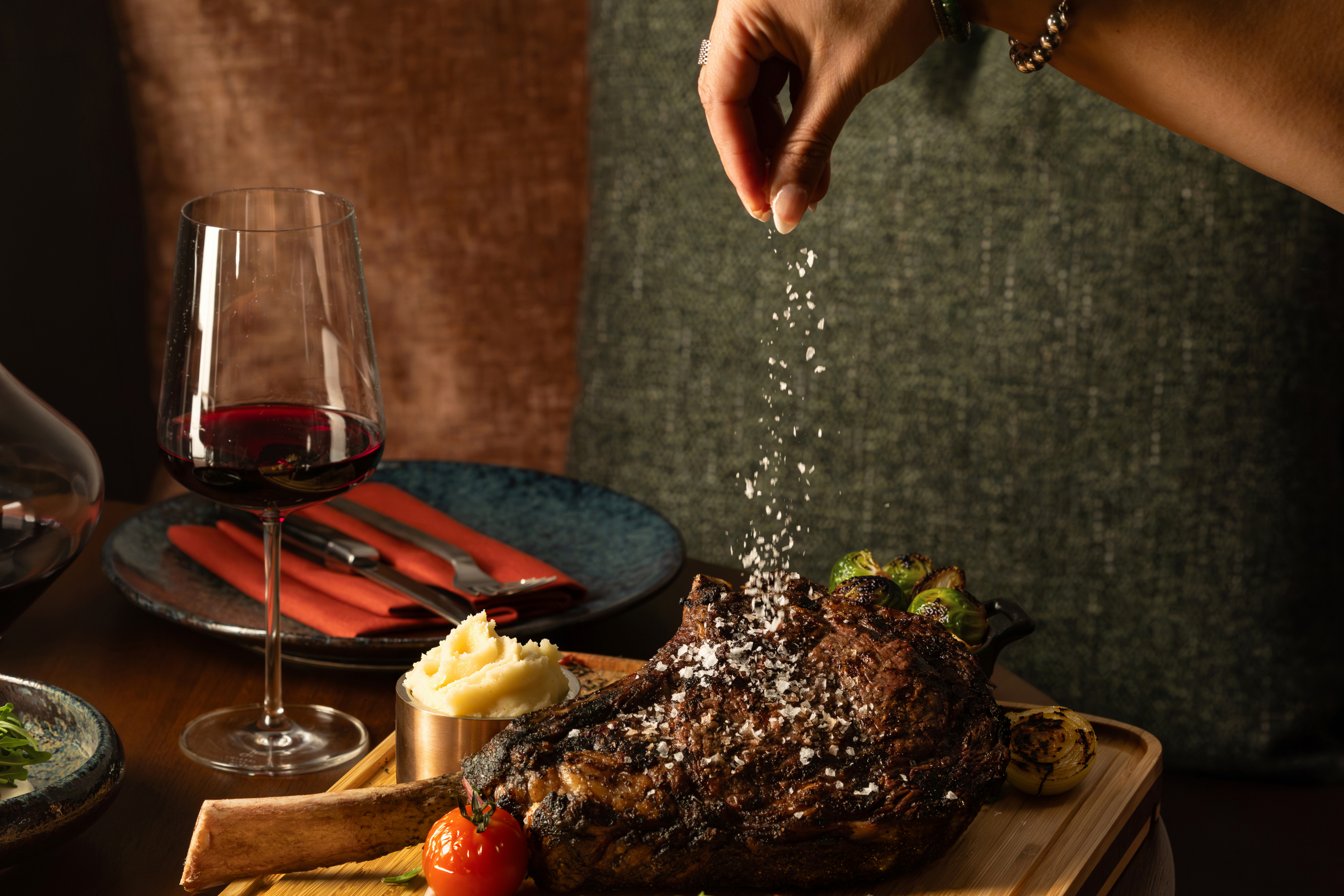 Woman's hand sprinkling salt on a cooked tomahawk steak.