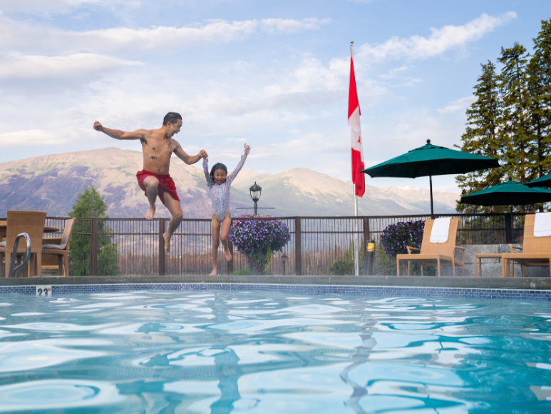 A father and daughter jumping into a swimming pool.