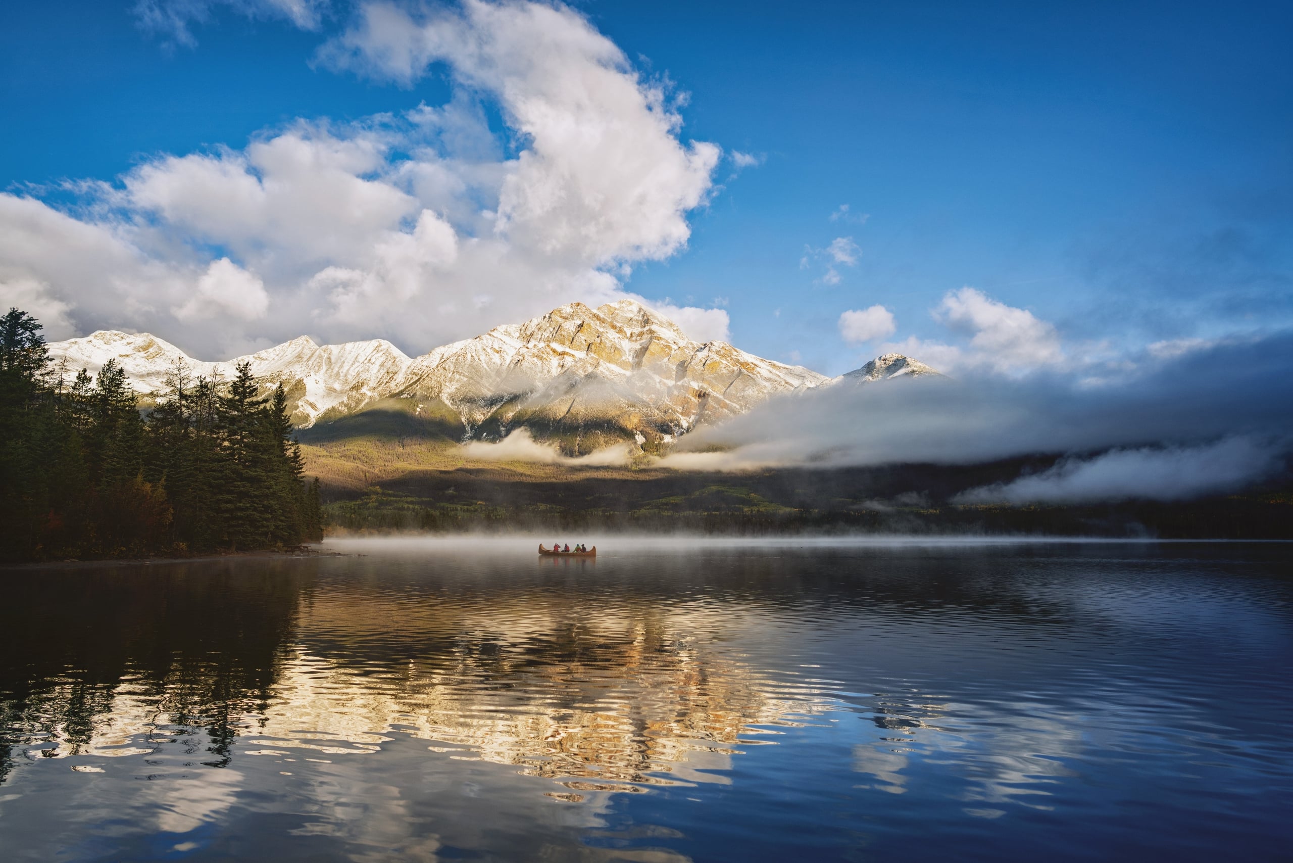 Passengers in a canoe on a lake surrounded by mountains and trees